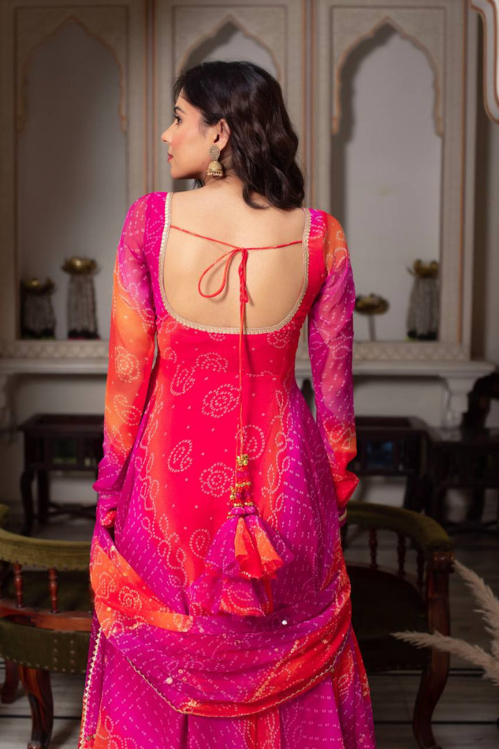 Woman wearing a vibrant pink and orange traditional outfit with intricate patterns in an indoor setting.