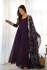 Woman wearing a long purple dress with a floral dupatta in a bright room.
