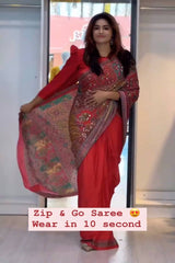 Woman in a red saree with a decorative border, standing indoors.