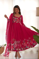 Woman wearing a pink floral dress with a matching dupatta in a bright room.