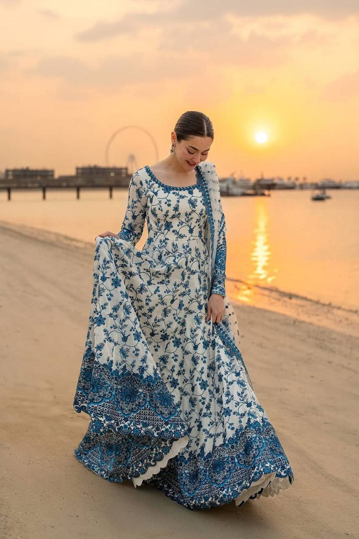 Woman in a blue and white floral dress standing on a beach at sunset.