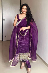 Woman wearing a purple traditional outfit with a matching dupatta indoors.