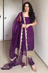 Woman wearing a purple traditional outfit with a matching dupatta indoors.