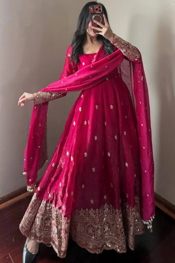Person wearing a red traditional outfit with gold embroidery in a room.
