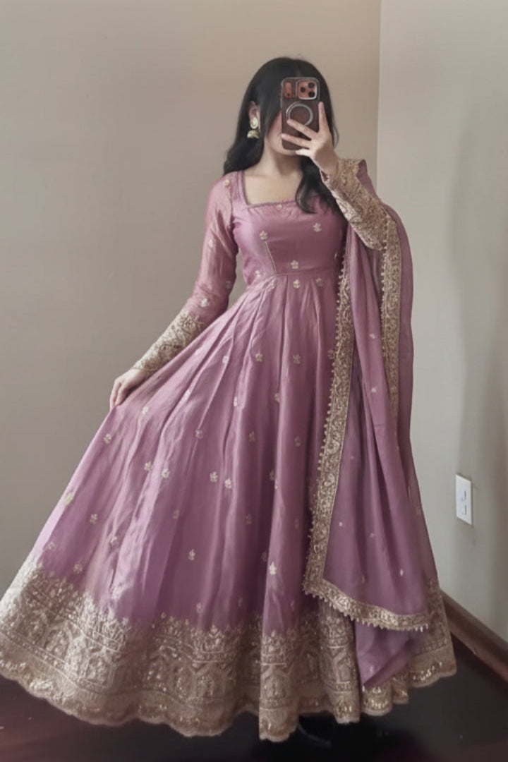 Person wearing a pink traditional outfit with gold embroidery in a room.