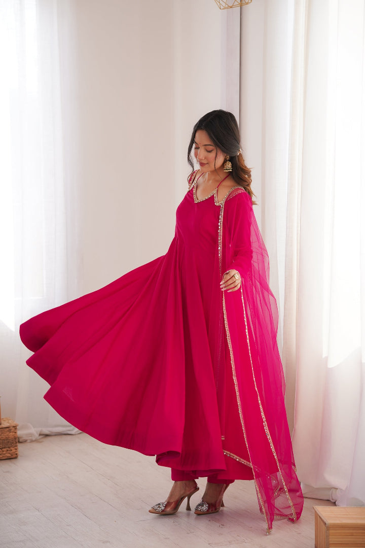 Woman in a bright pink traditional outfit with a sheer dupatta in a well-lit room.