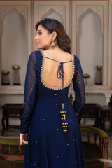 Woman wearing a dark blue dress with intricate detailing in an ornate room.