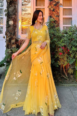 Woman in a yellow saree with floral patterns standing outdoors.