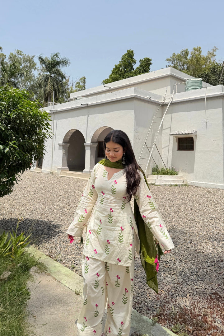 Woman in a floral outfit standing in front of a white building with greenery around.