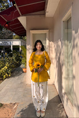 Woman in a yellow outfit holding sunflowers standing outside a building.
