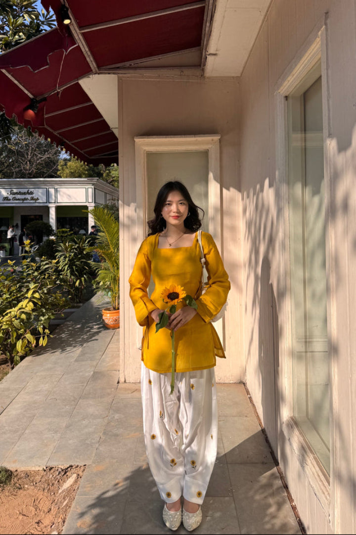 Woman in a yellow outfit holding sunflowers standing outside a building.