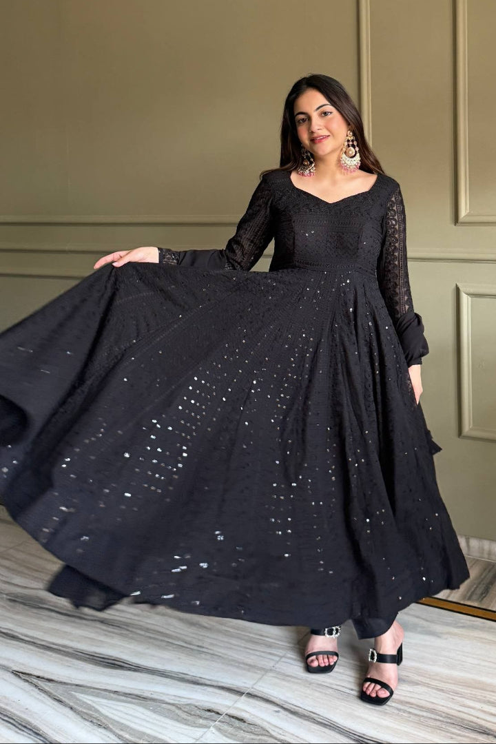 Woman holding a black dress with sequin details in a room with a neutral wall and marble floor.