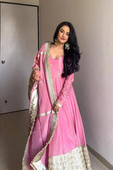 Woman in a pink traditional outfit with gold details against a plain wall.