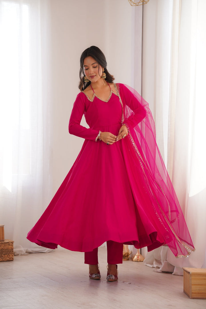 Woman wearing a bright pink traditional outfit with a flowing design in a softly lit room.
