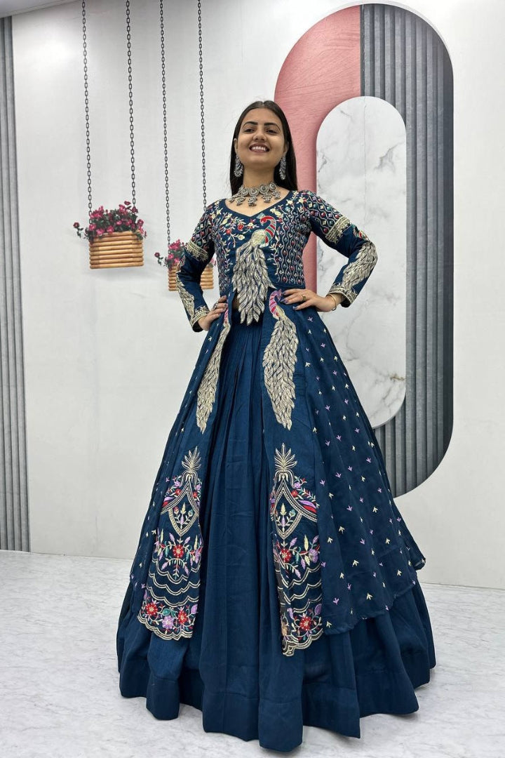 Woman in a dark blue embroidered dress standing indoors with a decorative background.