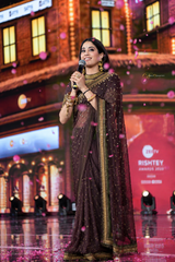 Woman in a saree holding a microphone on a stage with a blurred background