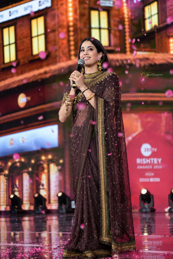 Woman in a saree holding a microphone on a stage with a blurred background