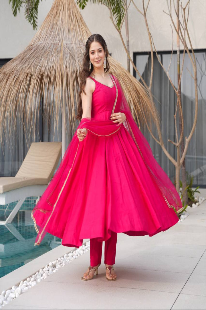 Woman in a bright pink traditional outfit standing by a poolside with greenery in the background