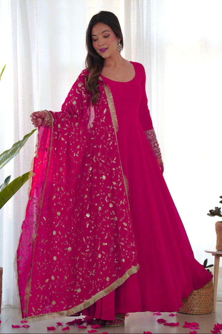 Woman in a bright pink traditional outfit with a matching dupatta, standing indoors.