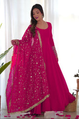 Woman in a bright pink traditional outfit with a matching dupatta, standing indoors.