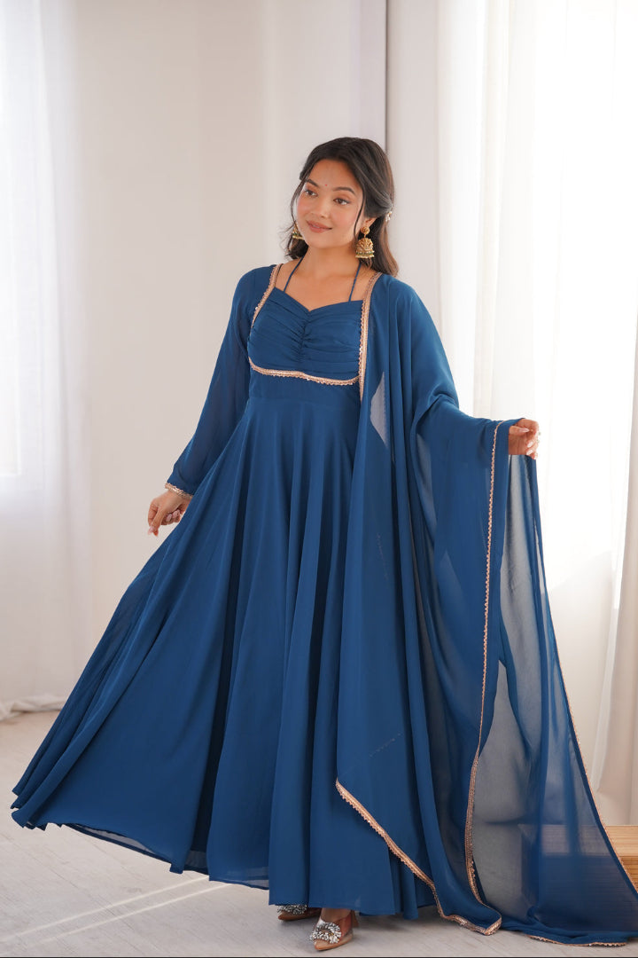 Woman wearing a long blue dress with a matching shawl in a bright room.