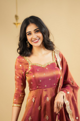 Woman wearing a traditional maroon and gold outfit with a beige background