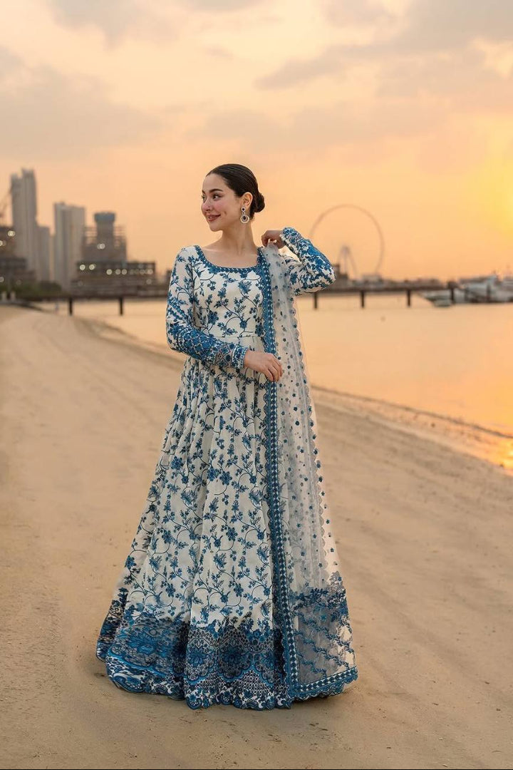 Woman in a blue and white floral dress standing on a beach with a city skyline in the background.