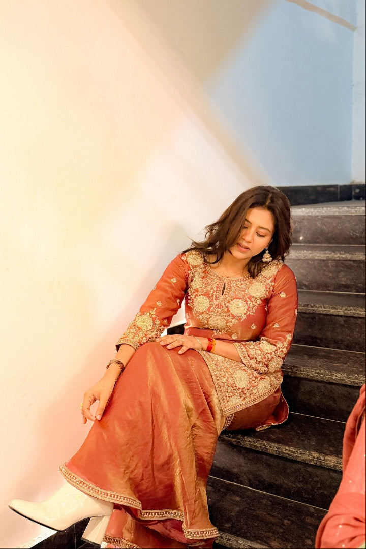 Woman in traditional outfit sitting on steps with a light background