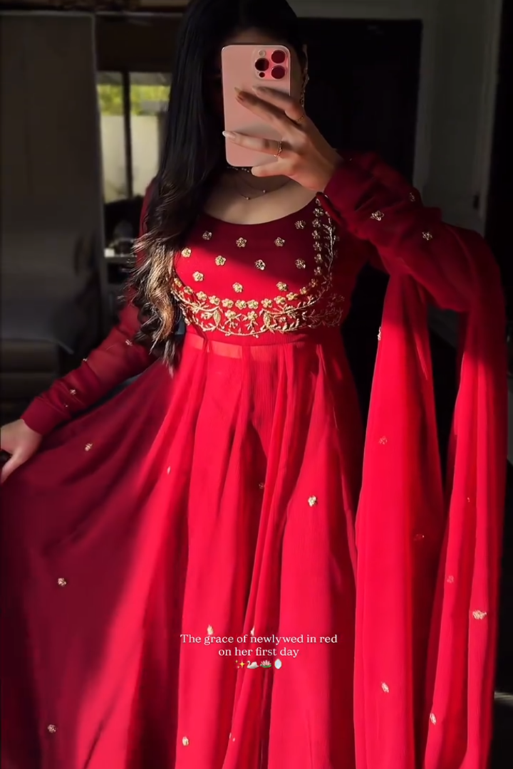 Person wearing a red traditional outfit with gold details, taking a mirror selfie.