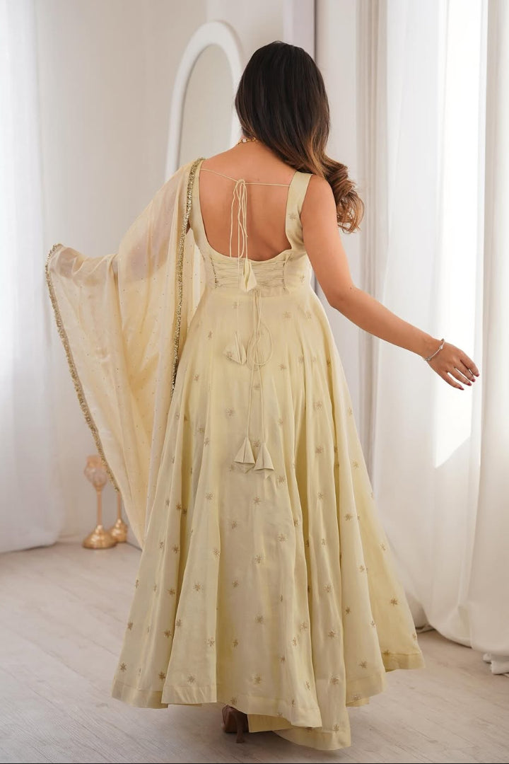 Woman in a light yellow dress standing in a bright room with white curtains.