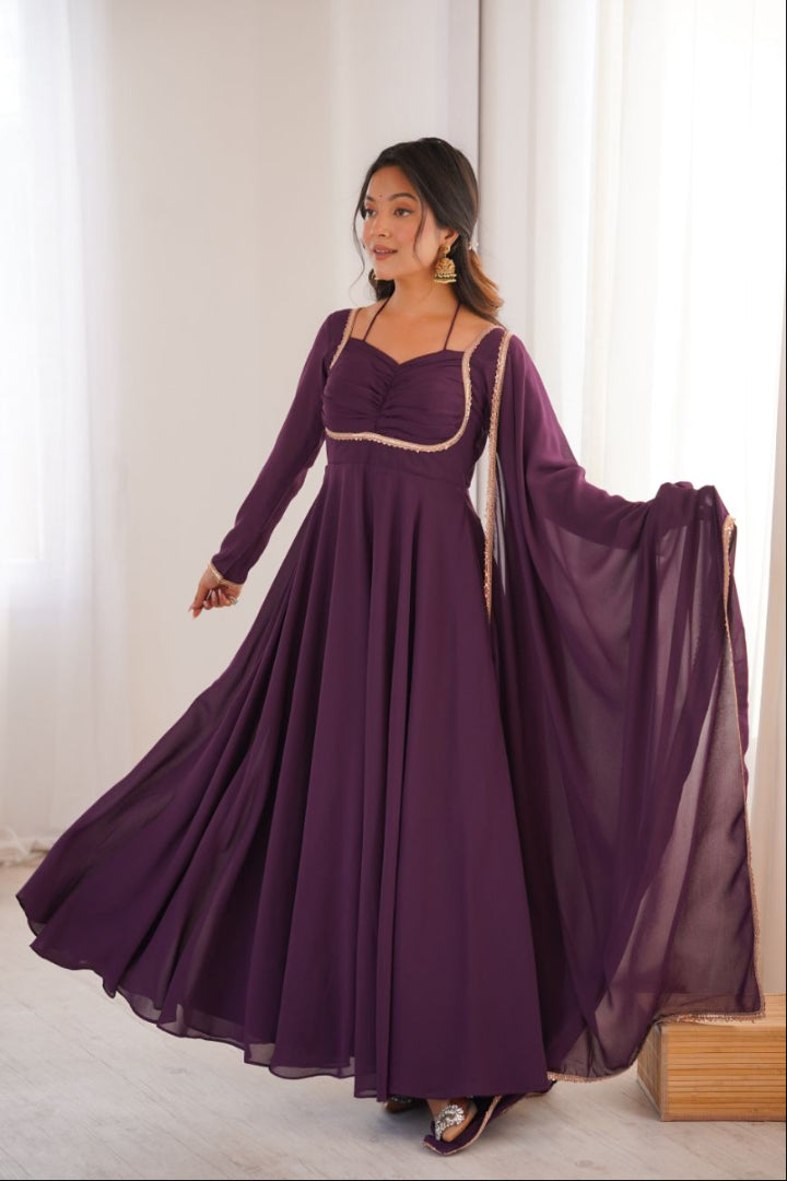 Woman wearing a long purple dress with a sheer overlay in a bright room.