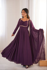 Woman wearing a long purple dress with a sheer overlay in a bright room.