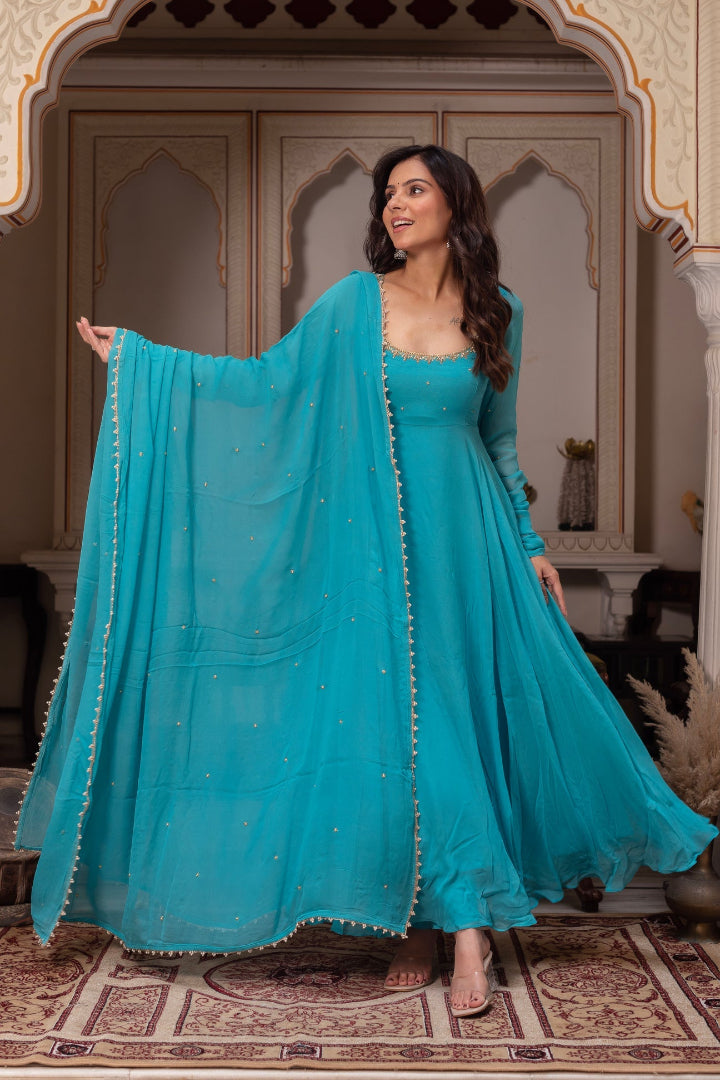 Woman in a turquoise traditional outfit with a matching dupatta in an ornate room.