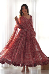 Woman wearing a red floral dress standing in a bright room with white curtains.