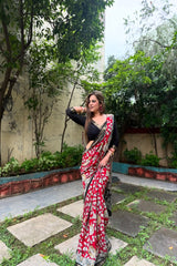 Woman in a red and white saree standing in a garden with greenery around.