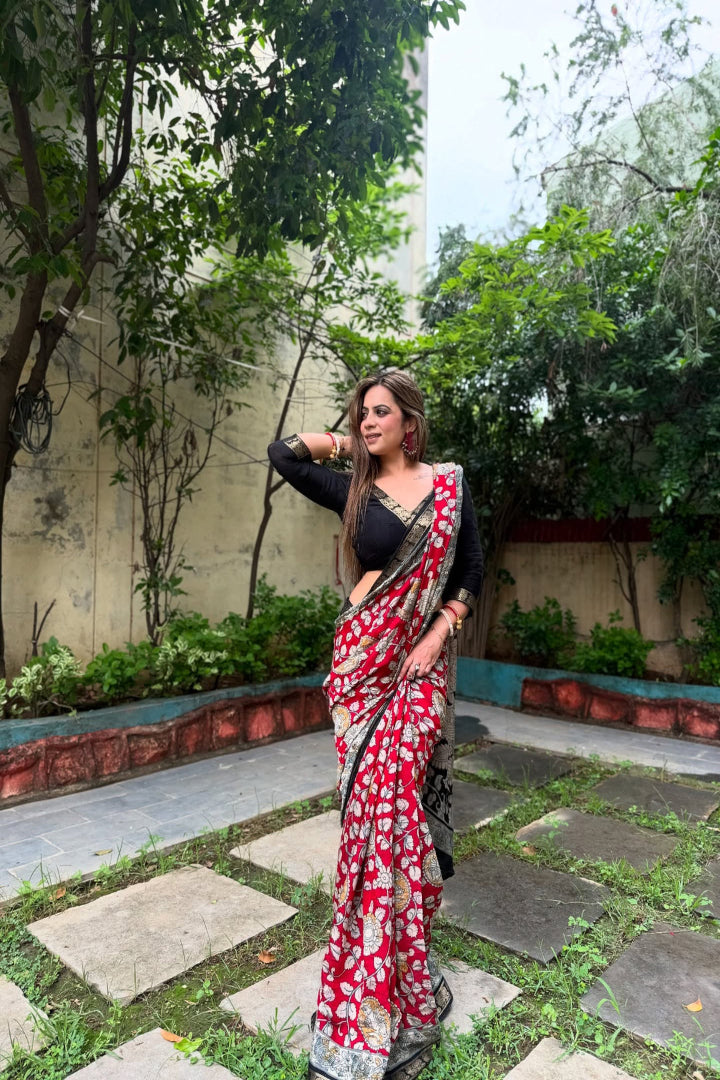 Woman in a red and white saree standing in a garden with greenery around.