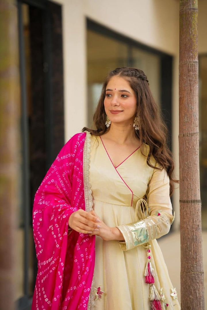 Woman in a cream traditional outfit with a pink dupatta standing outdoors.