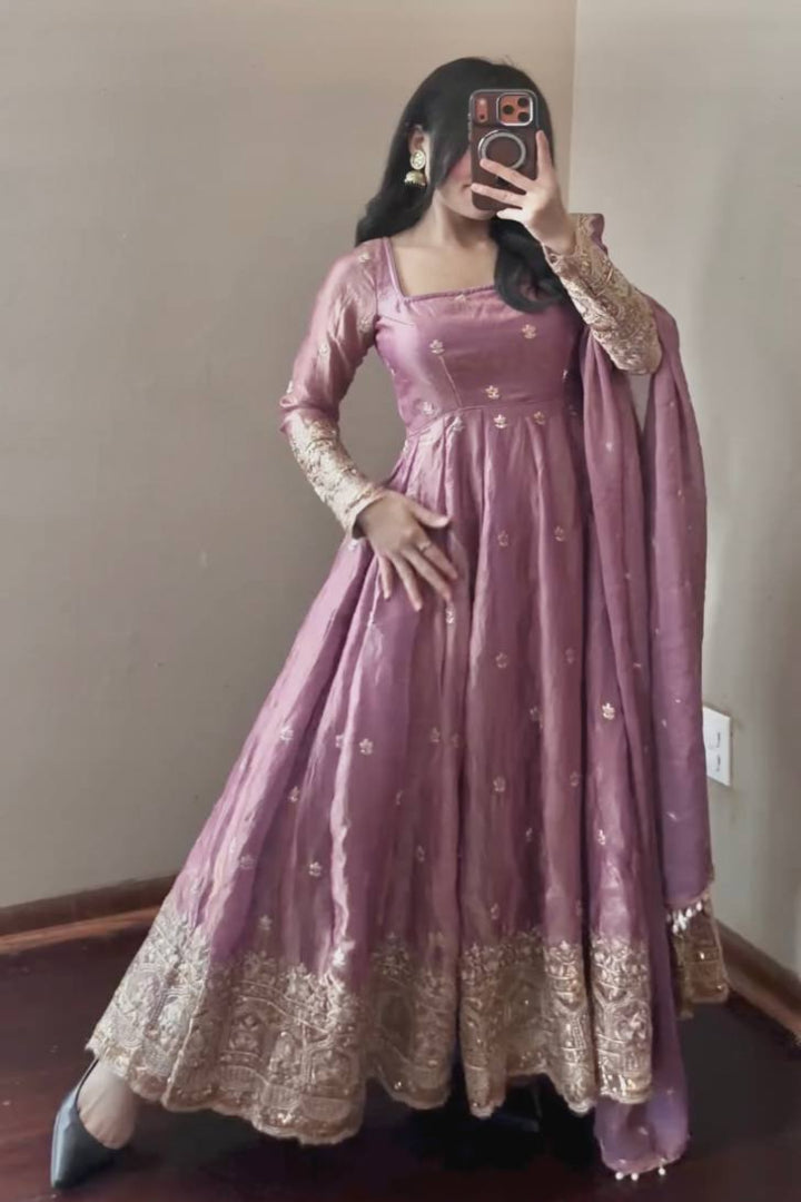 Person wearing a pink anarkali suit with gold embroidery in a room.