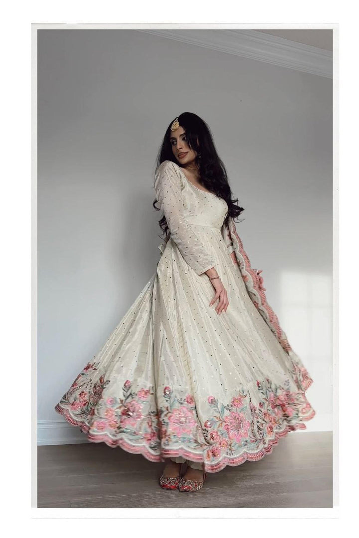 Woman wearing a long, floral embroidered dress against a plain background