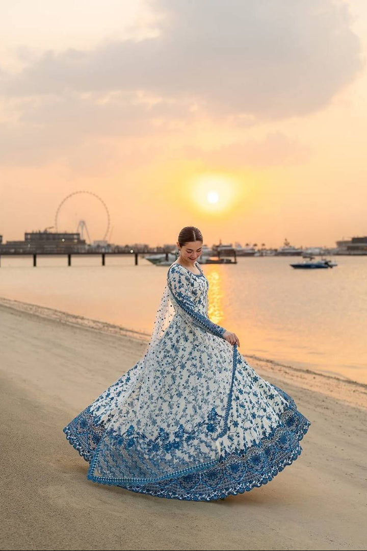 Woman in a blue and white dress standing on a beach at sunset.