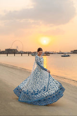 Woman in a blue and white dress standing on a beach at sunset.