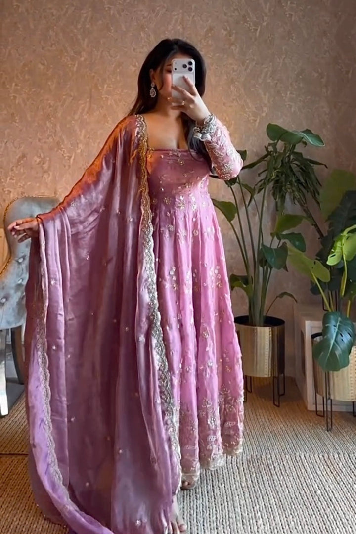 Person wearing a pink traditional outfit with a long scarf in a room with plants.