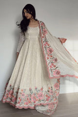 Woman wearing a cream-colored traditional outfit with floral embroidery on a plain background