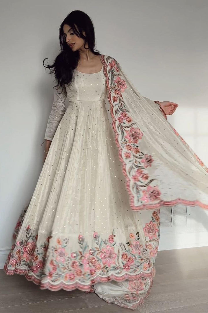 Woman wearing a cream-colored traditional outfit with floral embroidery on a plain background