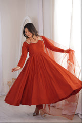 Woman in a red dress with a sheer overlay standing in a softly lit room.