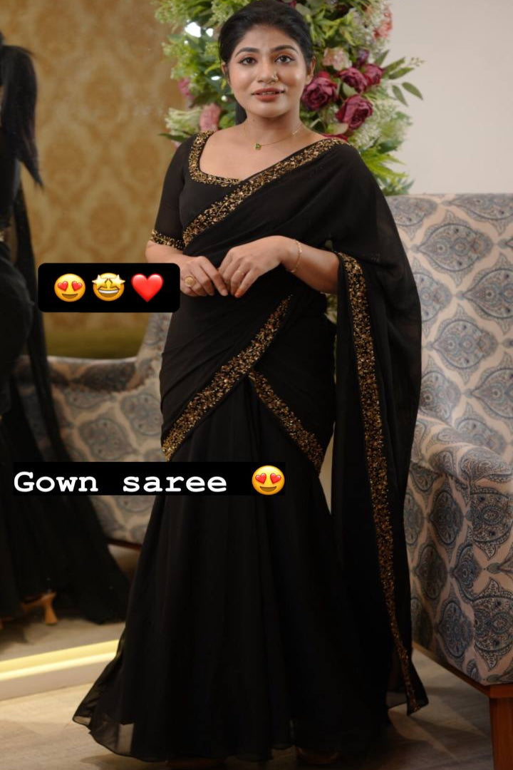 Woman wearing a black gown saree with decorative patterns in a decorated room.