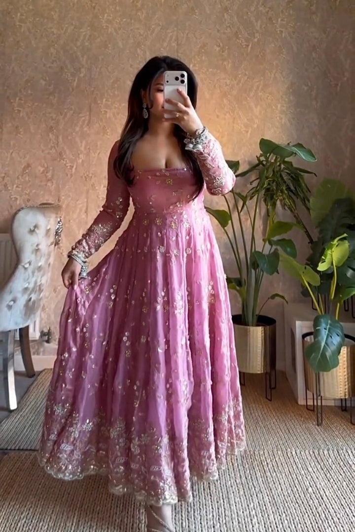 Woman taking a mirror selfie wearing a pink dress in a room with plants and a chair.
