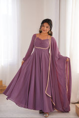 Woman wearing a long purple dress with a matching dupatta in a bright room.