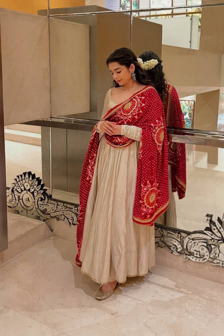 Woman in a red and white traditional outfit standing in a reflective indoor setting.