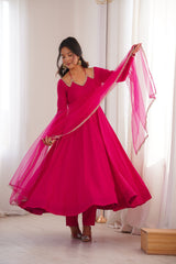Woman in a bright pink traditional outfit with a matching dupatta, standing indoors.